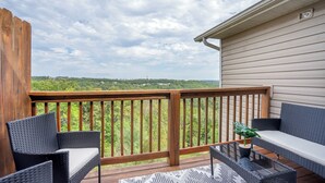 A wooden deck with wicker furniture and a glass table, overlooking a green landscape.