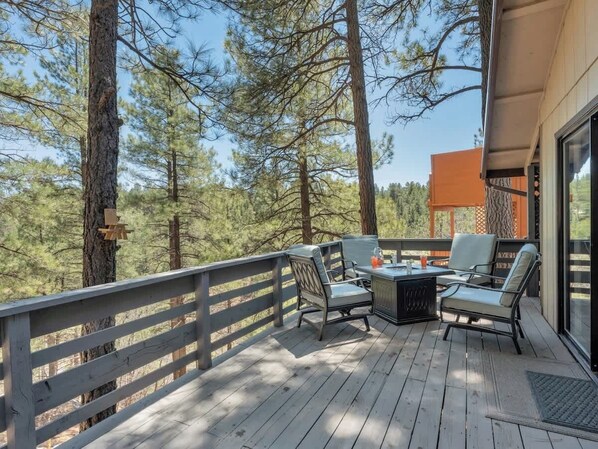 A deck with outdoor furniture, a table, and a view of the surrounding forest.