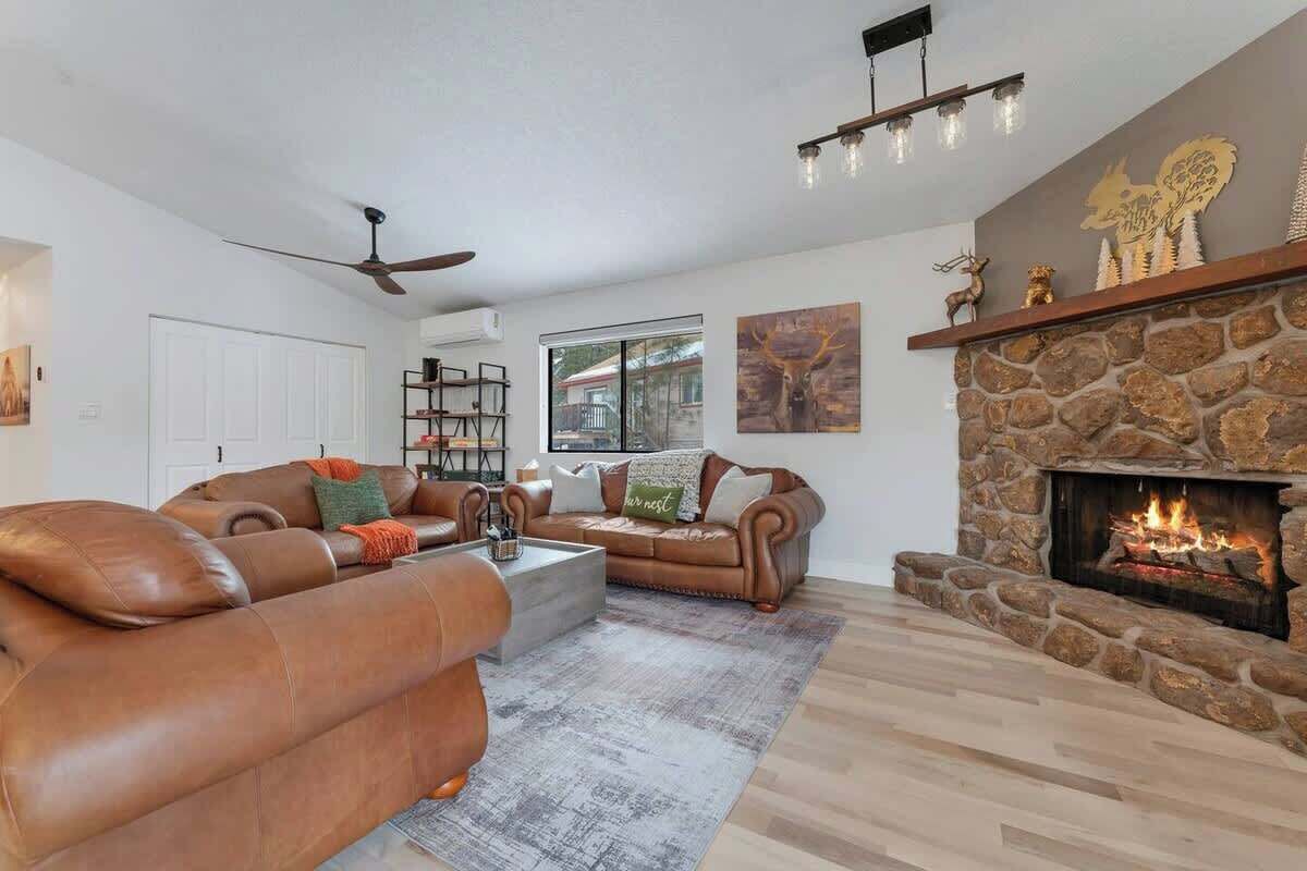 Una sala de estar con sofás de cuero, chimenea de piedra y ventilador de techo.