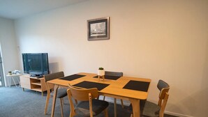 Un coin repas avec une table en bois, quatre chaises, un téléviseur posé sur un meuble et un tableau encadré accroché au mur.