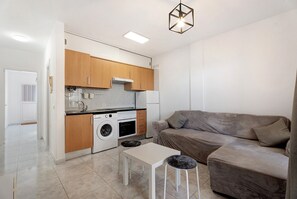 Een compacte keuken met houten kastjes, een wasmachine en een eethoek met een tafel en krukjes.