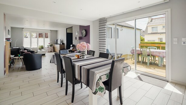 Un vaste espace de vie comprenant une table à manger, des chaises et une porte-fenêtre coulissante donnant sur une terrasse extérieure.