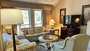 Een woonkamer met een bank, fauteuils, een salontafel, een televisie en een plafondventilator.