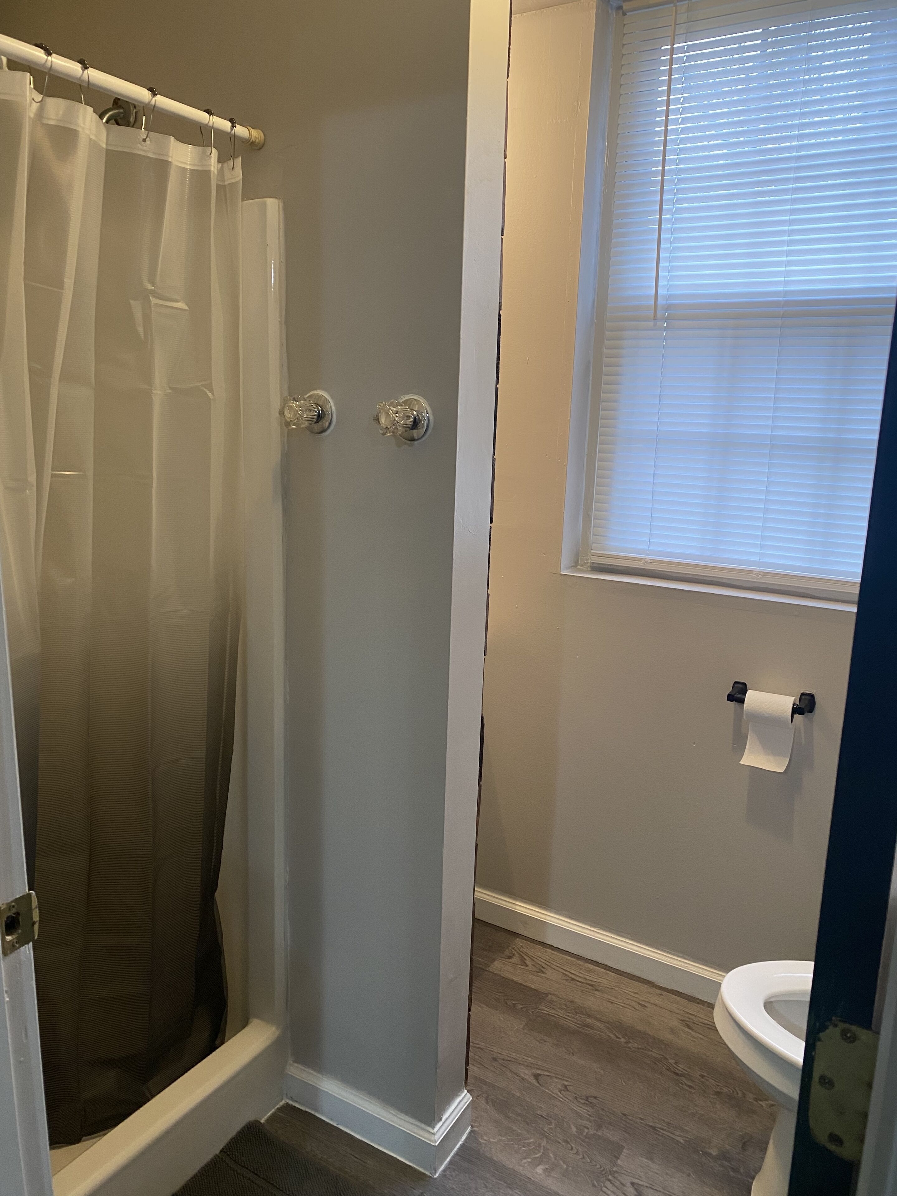 Ein Badezimmer mit Dusche, Toilette und Fenster.