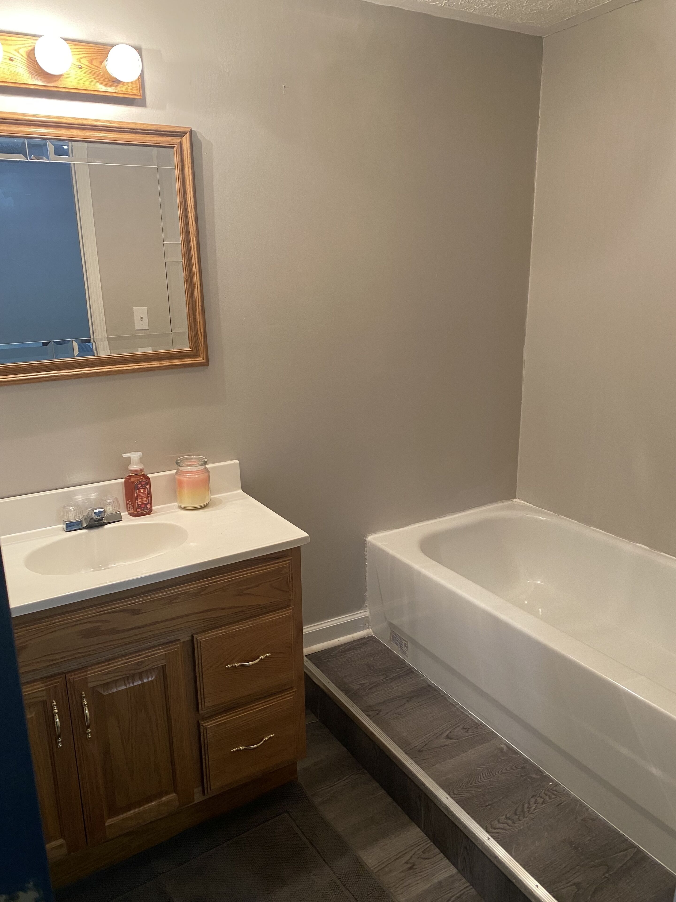 A bathroom with a white sink, wooden vanity, a large mirror, and a white bathtub.