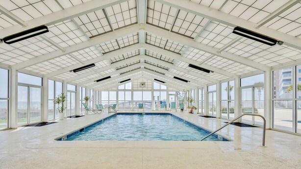 An indoor swimming pool with a high ceiling, large windows, and a view of the outside.