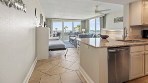 A modern kitchen with a dishwasher, a dining area with a table and chairs, and a view of the beach.