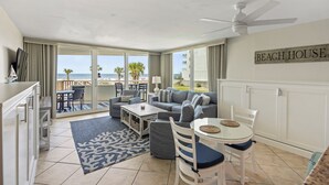 A beach house interior with a sofa set, dining table, and a ceiling fan.