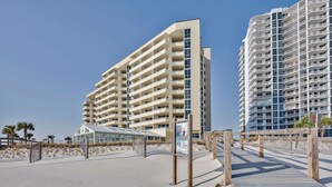 A beachfront hotel with multiple floors, a sandy beach area, and a wooden boardwalk.