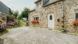 A stone building with a gravel driveway, a white door, and flower boxes. - Cottage 'Gite Les Dauphins À Matignon' with Private Terrace, Private Garden and Wi-Fi (Matignon)