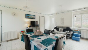 A dining area with a table set for four, a television, and a sofa in a living room. - Cottage 'Gite Les Dauphins À Matignon' with Private Terrace, Private Garden and Wi-Fi (Matignon)