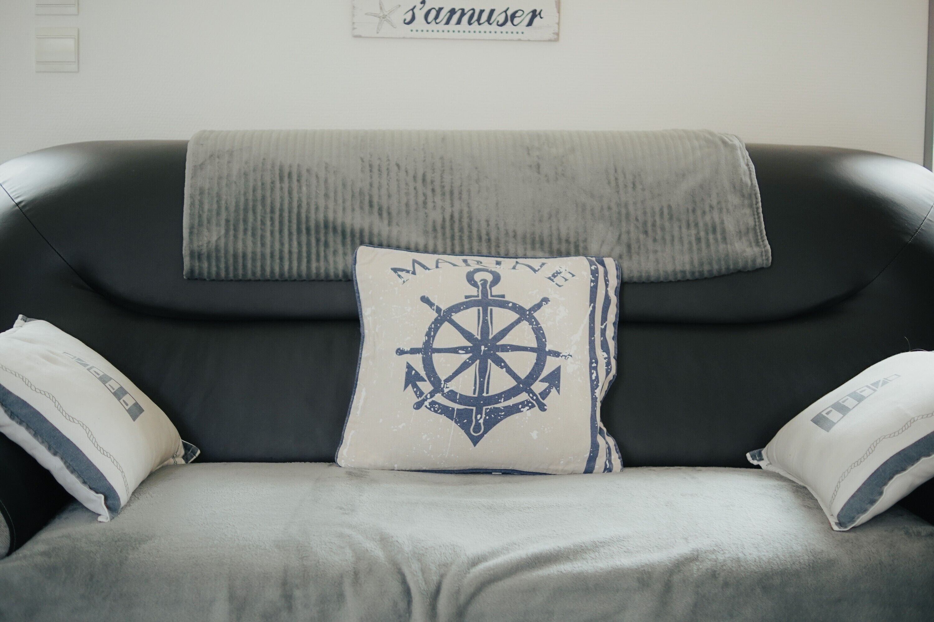 A black leather sofa with a nautical-themed pillow and a blanket.