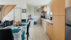 A compact kitchen with wooden cabinets, a dining area with a table set for two, and a staircase leading to another level. - Cottage 'Gite Les Dauphins À Matignon' with Private Terrace, Private Garden and Wi-Fi (Matignon)