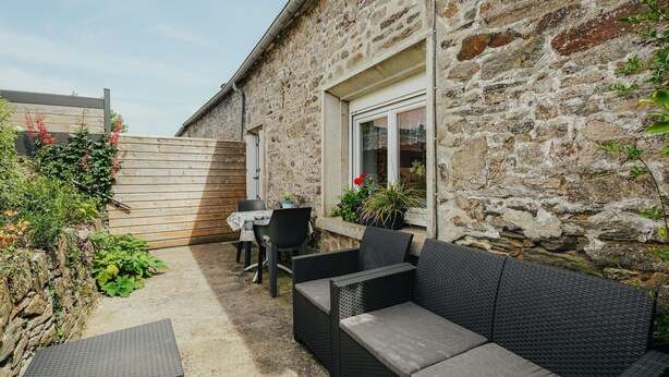 A stone building with a patio area featuring outdoor furniture and a table. - Cottage 'Gite Les Dauphins À Matignon' with Private Terrace, Private Garden and Wi-Fi (Matignon)