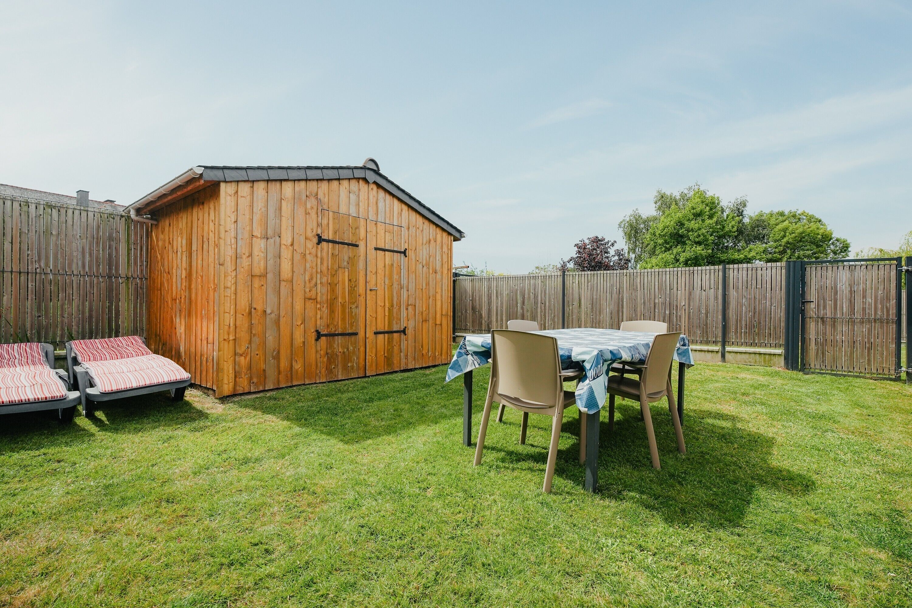 Ein Holler Schuppen, ein Tisch mit Stühlen und zwei Liegestühle in einem Garten.