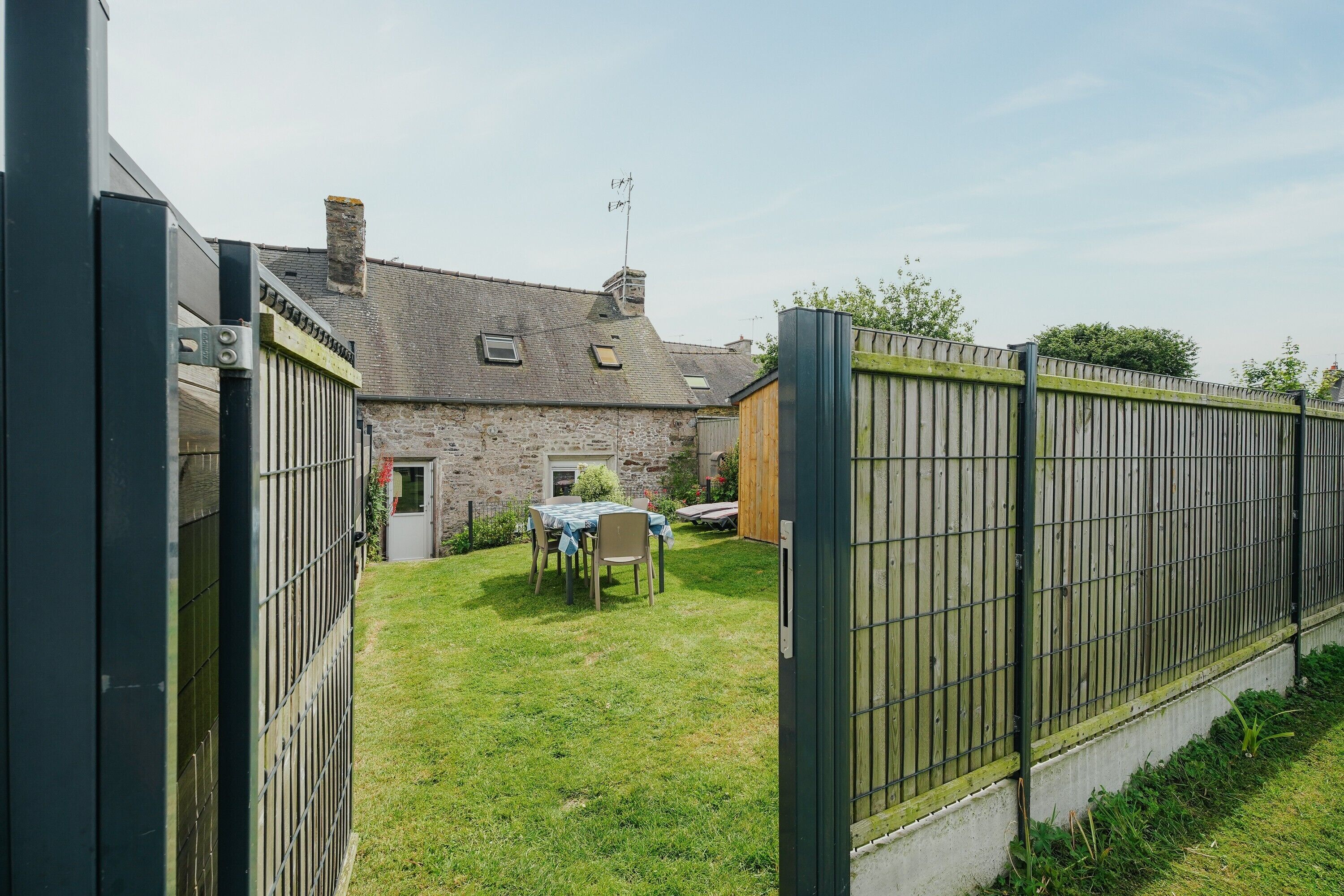 A stone building with a fenced yard, a table with chairs, and a small garden.