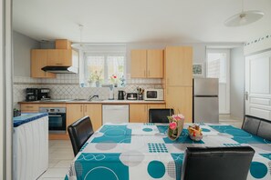 Une cuisine moderne avec des meubles en bois, une table à manger recouverte d’une nappe bleue et blanche, et un réfrigérateur.