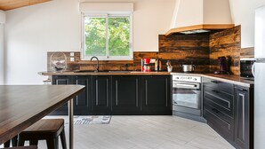 Una cucina moderna con mobili scuri, soffitto in legno, un'ampia finestra e forno a incasso.