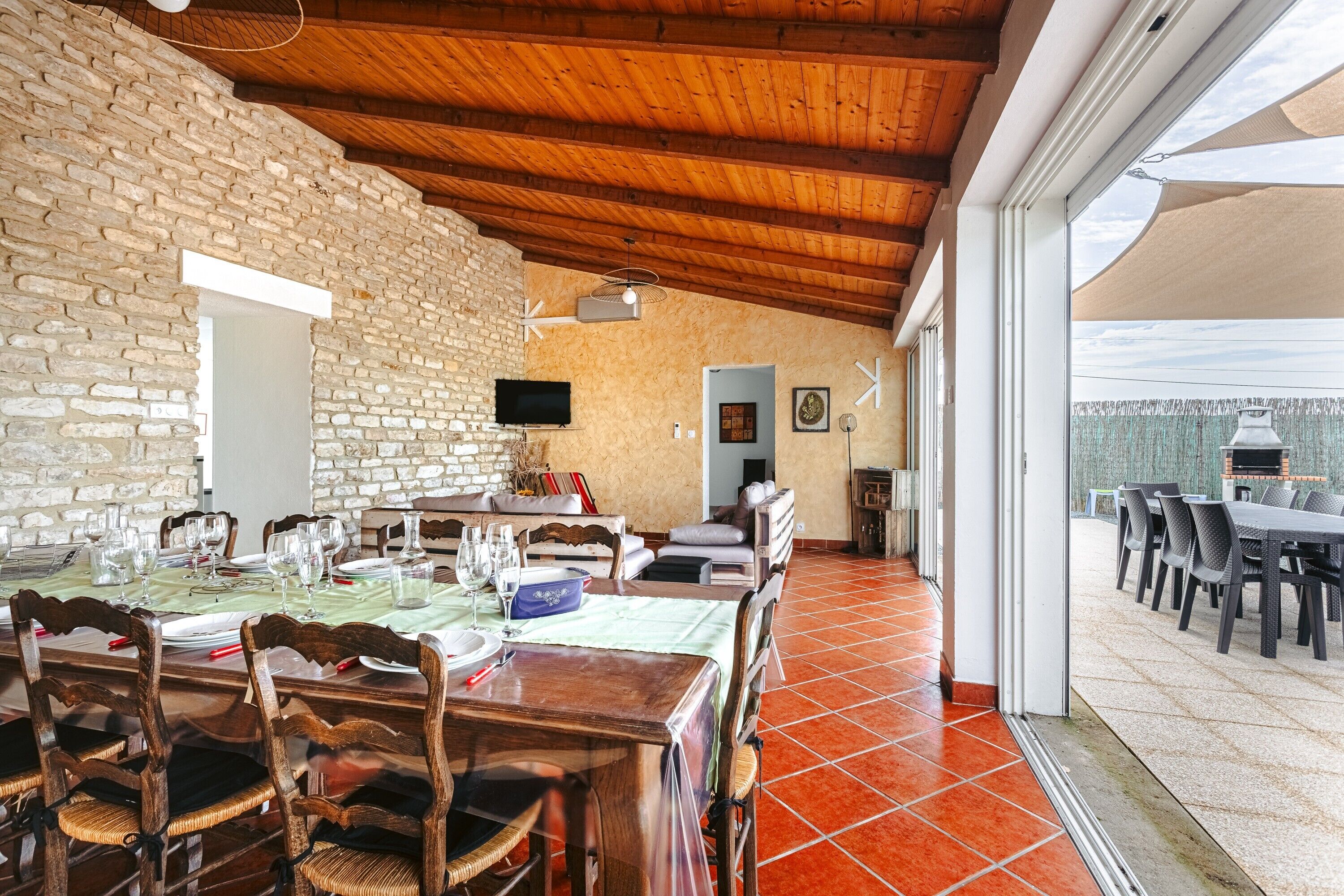 A dining area with wooden tables and chairs, a stone wall, and a television.