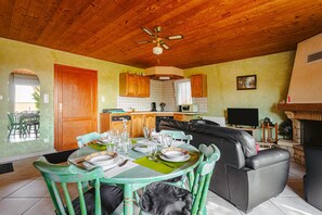 A dining area with a wooden ceiling, a kitchen in the background, and a living area with a fireplace. - Holiday Home 'Gîte Le Petit Sableau' with Shared Pool & Spa, Private Terrace, Wi-Fi (MARANS)