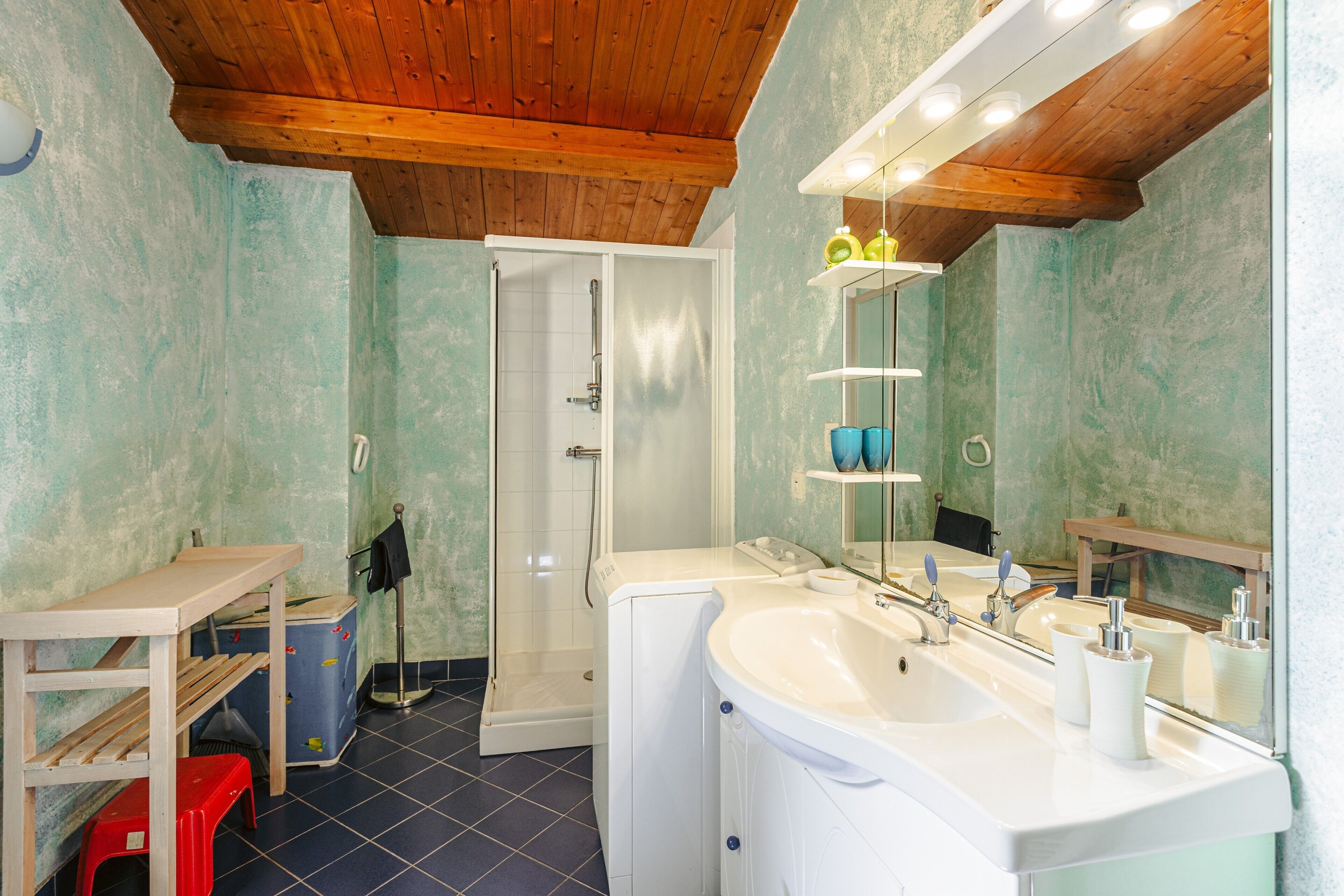 Een badkamer met een houten plafond, een groot wastafel, een spiegel en een douche.