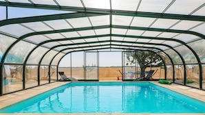 A covered swimming pool with clear blue water, surrounded by lounge chairs and a glass enclosure. - Holiday Home 'Gîte Le Petit Sableau' with Shared Pool & Spa, Private Terrace, Wi-Fi (MARANS)