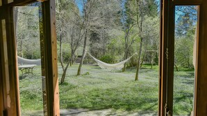 A view through a window of a room with a hammock, a table, and a path leading to a staircase in a wooded area. - La Bergerie de Montcuq – Private Pool & Jacuzzi, Panoramic Views (Montcuq-en-Quercy-Blanc)