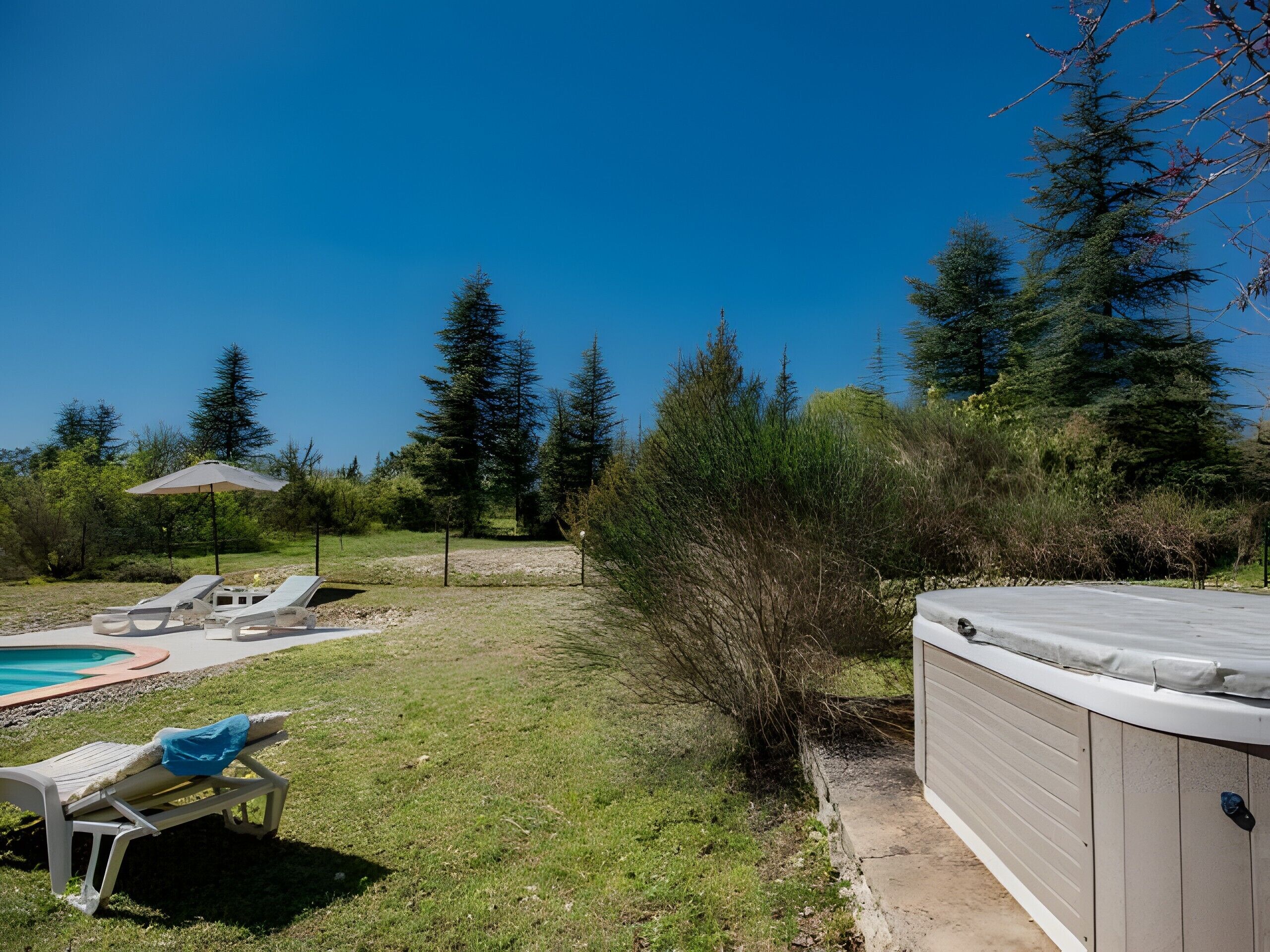 Un patio trasero con un jacuzzi, sillas de descanso y una piscina.