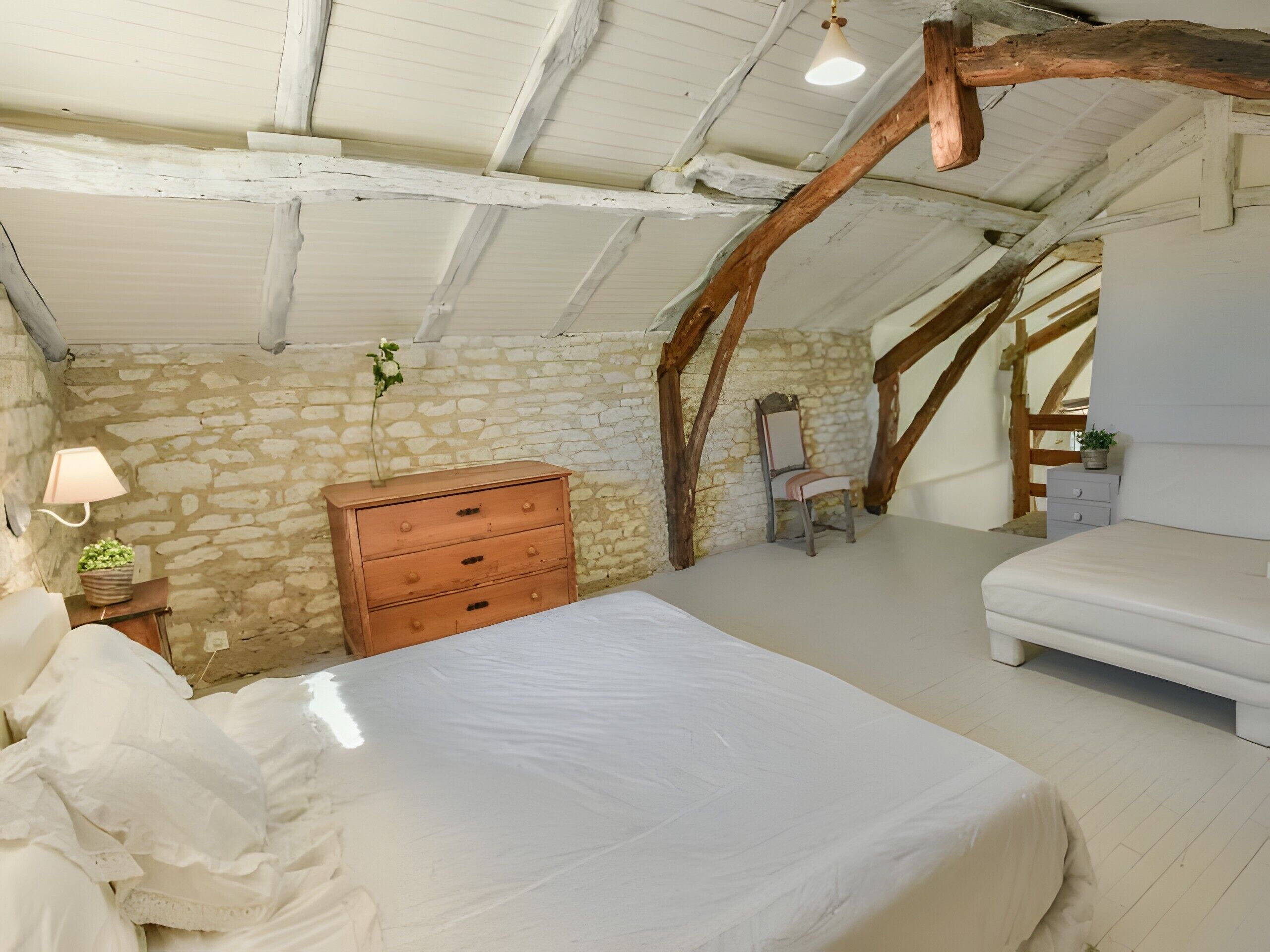 Une chambre à coucher avec un lit, une commode, une chaise et un mur en pierre.