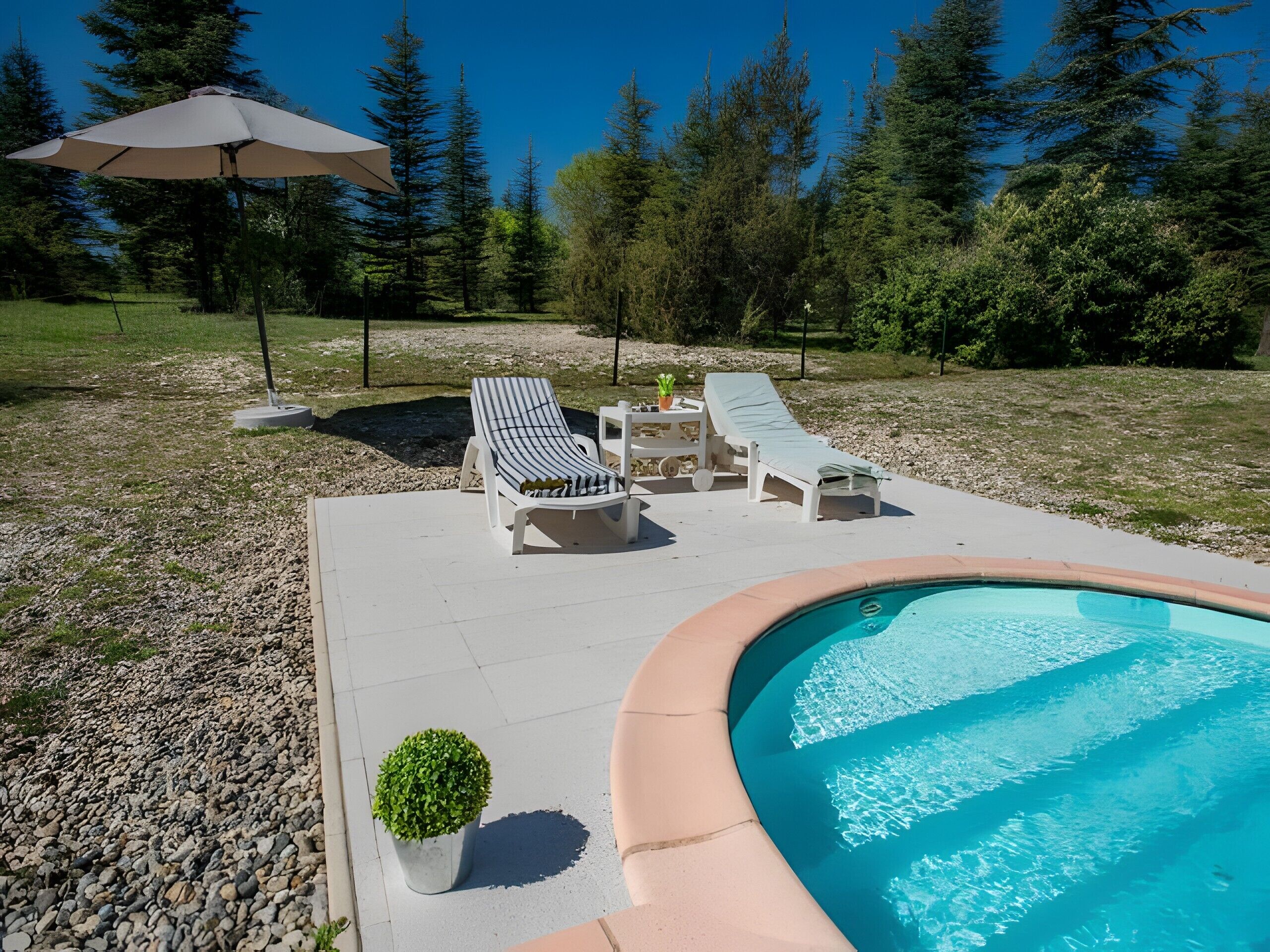 A swimming pool with lounge chairs and umbrellas, surrounded by trees.