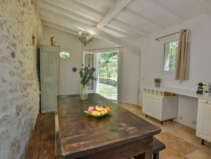 A rustic kitchen with a wooden table, a vase with flowers, and a fruit bowl.
