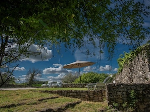 A stone wall, a stone bench, and a white umbrella in a garden.