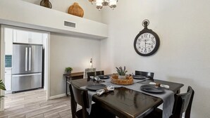 A modern kitchen with a stainless steel refrigerator, a dining table set with plates and a centerpiece, and a wall-mounted clock. - 4 Bed Shuffleboard& Private Pool Retreat in Peoria (Peoria)