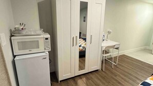 Una habitación compacta con un armario blanco, un refrigerador pequeño, un microondas, una cama individual y una silla.