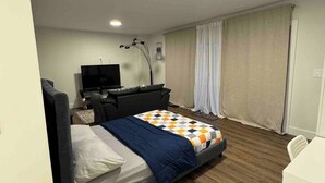 Un dormitorio moderno con cama, escritorio, silla, televisor y ventana con cortinas.