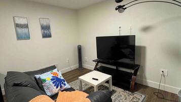 A living room with a black sofa, a white coffee table, a TV, and a patterned rug.