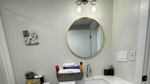 Un baño con inodoro, lavabo y espejo. Se observa una decoración de estrella de mar en la pared, una cesta de artículos de aseo y un cubo de basura.