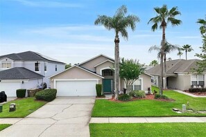 A residential neighborhood with single-family homes, a well-maintained lawn, and palm trees.