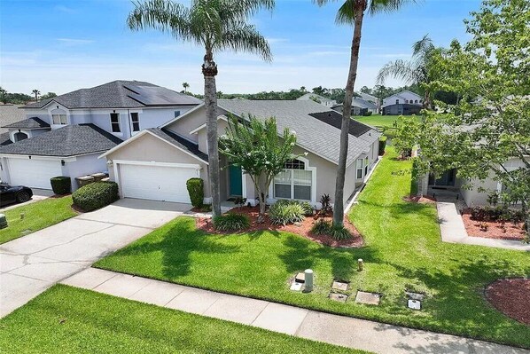 A residential neighborhood with houses featuring gabled roofs, front yards with grass, and palm trees.