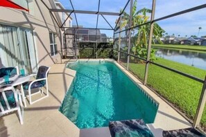 A swimming pool with a glass enclosure, surrounded by a patio area with chairs and a table.