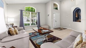 Uma sala de estar moderna com sofá, mesa de centro e uma janela grande com cortinas.