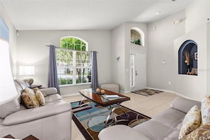 A modern living room with a sofa, coffee table, and a large window with curtains.