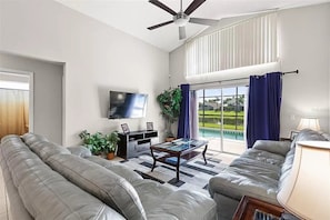 A modern living room with a flat-screen TV, leather sofas, a coffee table, and a ceiling fan.