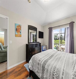 A bedroom with a bed, dresser, TV, and a window with curtains.