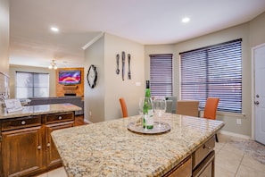 A kitchen with granite countertops, wooden cabinets, a dining area with a table and chairs, and a TV mounted on the wall.