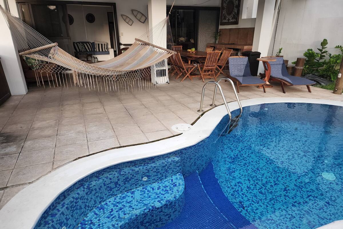 Ein Schwimmbecken mit gefliestem Rand, einer Hängematte und Gartenmöbeln.