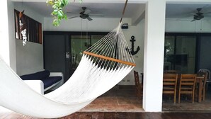 A hammock in a spacious room with wooden flooring, a ceiling fan, and a dining area visible through a glass door. - Los Cabos Monterrico byLAurora Inn (Taxisco)