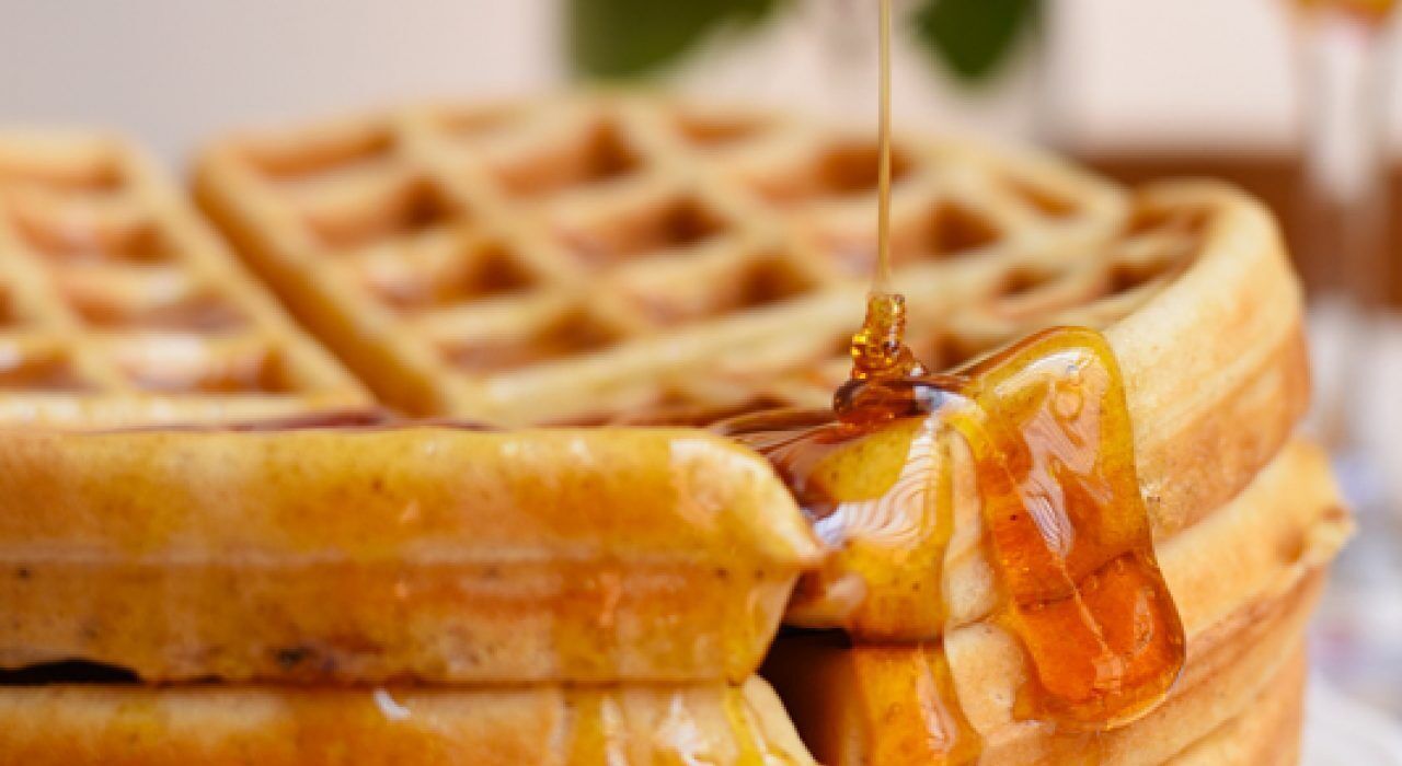 A close-up of a waffle with syrup being poured over it.