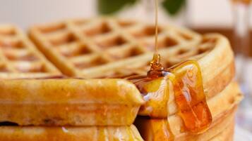 A close-up of a waffle with syrup being poured over it.