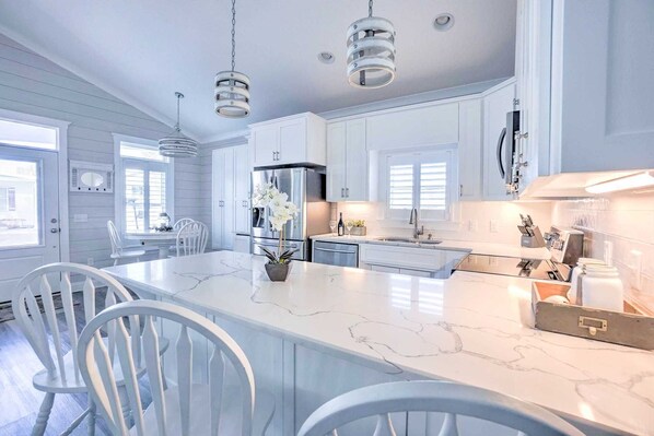 A modern kitchen with white cabinetry, a marble island, and pendant lighting.